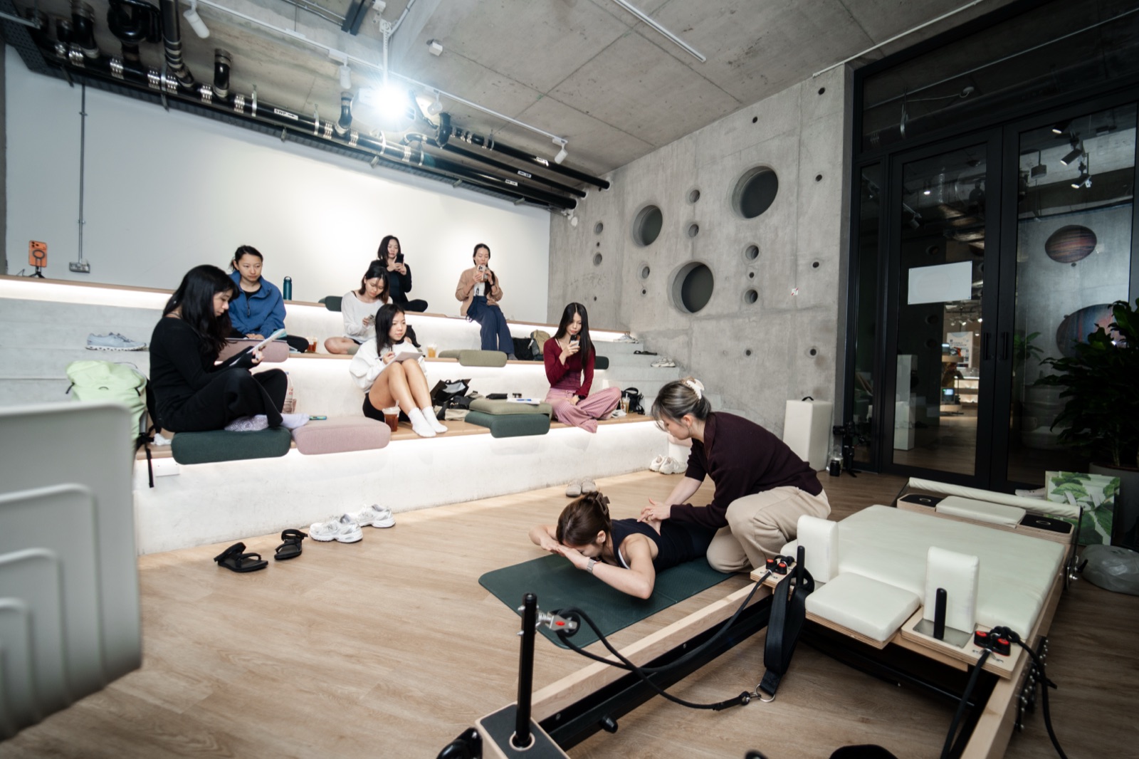 PX3 Cohort 1 in session — instructors observing from the studio's tiered seating while Julie demonstrates a correction on the mat